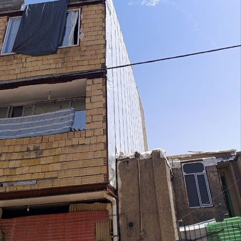 Missile or rocket contrails visible in a clear blue sky above a residential building with brick walls and tarp-covered windows, suggesting an interception or launch event in a Middle Eastern urban area.