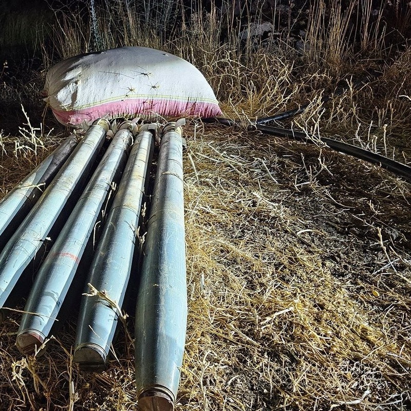 Several rocket or missile tubes, likely from a multiple rocket launcher system, lying on dry grass at night alongside sandbags, suggesting a seized or abandoned weapons cache.