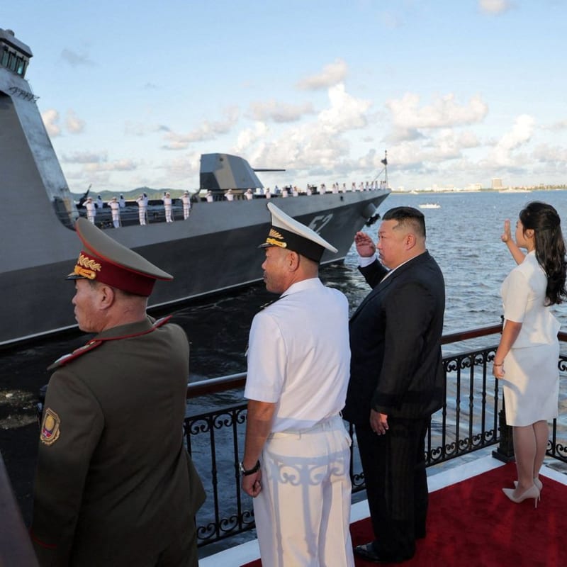North Korean leader Kim Jong Un, accompanied by his daughter and military officials in uniform, salutes a naval warship with sailors lined up on deck during what appears to be a North Korean navy review ceremony. The image is credited to KCNA (Korean Central News Agency).