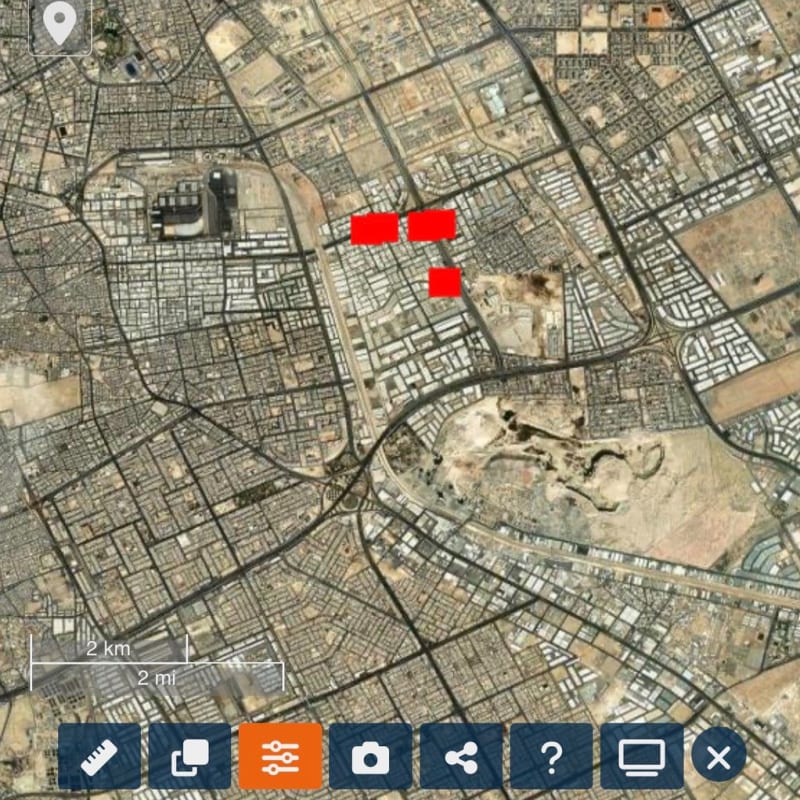 Satellite imagery screenshot of an arid Middle Eastern city, likely Riyadh, Saudi Arabia, viewed in a mapping application with red markers indicating specific locations and UI controls visible at the edges.
