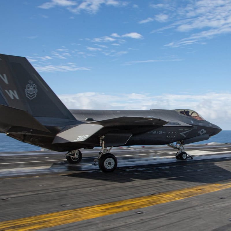 An F-35C Lightning II stealth fighter jet from VMFA-314, marked with tail number 312 and VW tail codes, launches from the flight deck of an aircraft carrier at sea under partly cloudy skies.