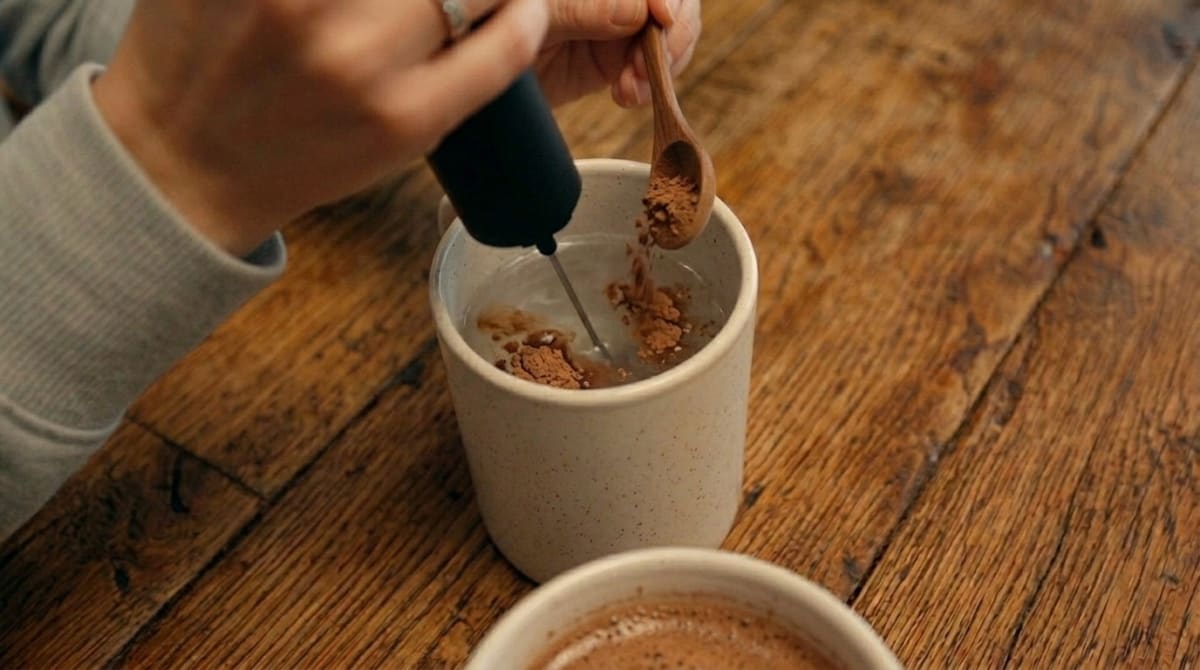 A person mixing mushroom coffee powder into hot water with a handheld frother