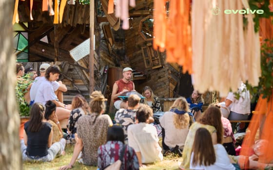 Teilnehmer des Evolve Festivals sitzen auf dem Boden und hören einem Musiker zu