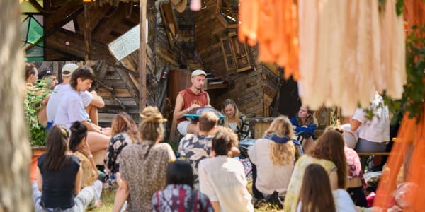 Teilnehmer des Evolve Festivals sitzen auf dem Boden und hören einem Musiker zu
