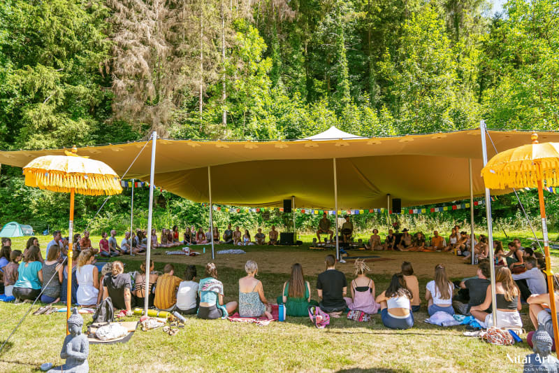 Teilnehmer der Summer Celebration sitzen im Kreis unter einem Zelt in der Natur und lauschen der Live-Musik