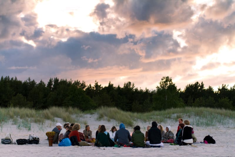 Teilnehmer des Space of Love Festivals sitzen gemeinsam im Kreis am Strand unter dem Abendhimmel