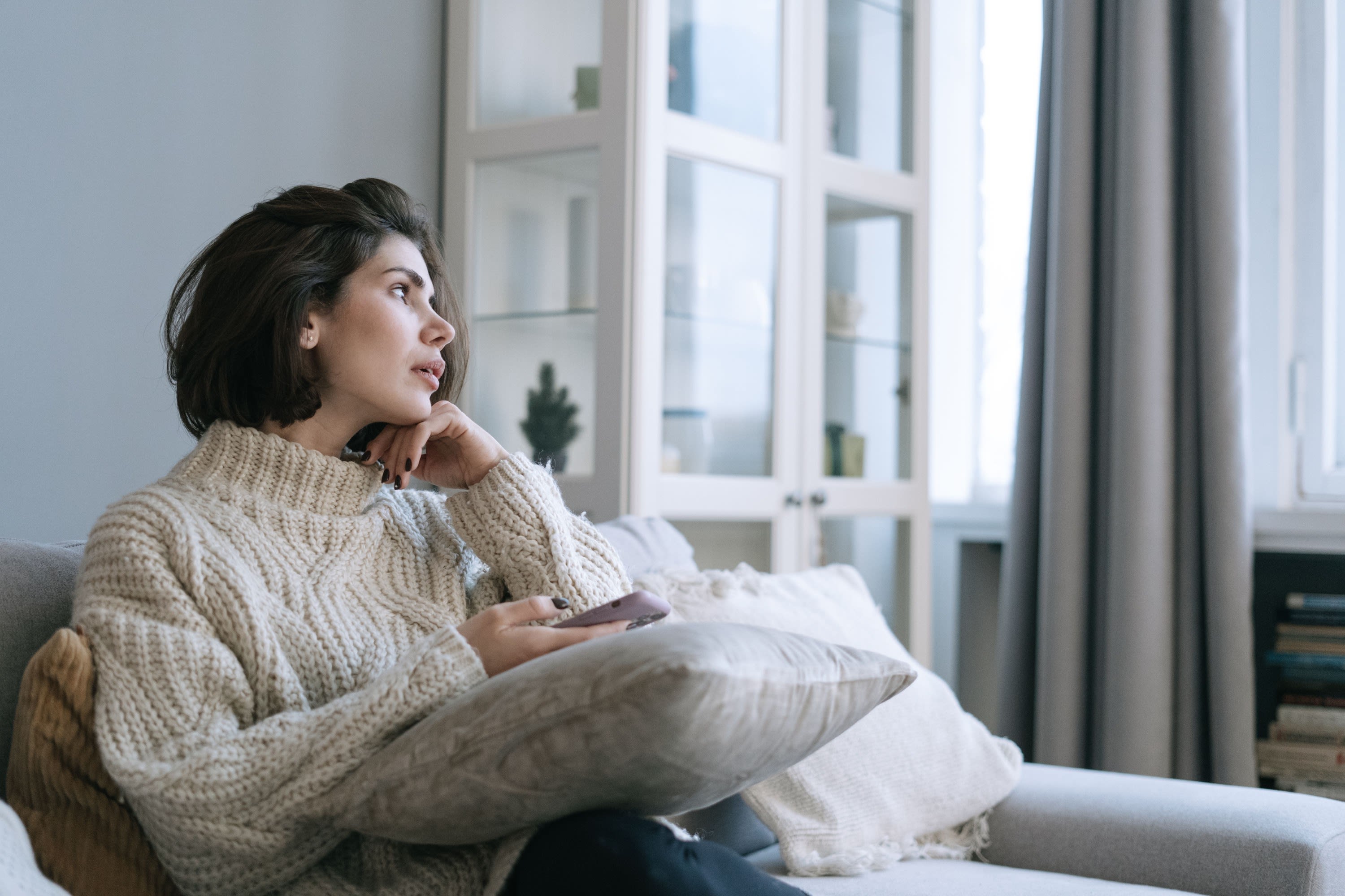 Woman at home pausing to think, phone in hand