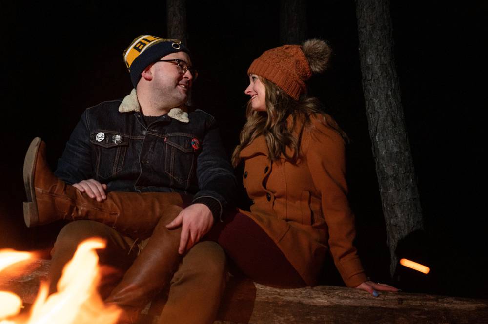 couple sitting on log in front of fire
