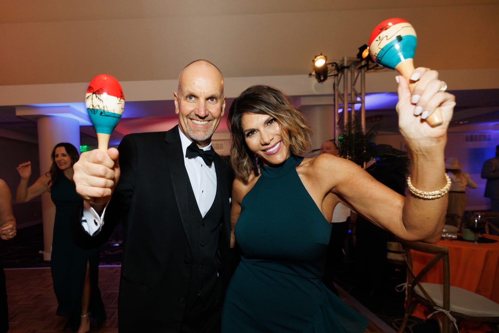 A couple holds up colorful maracas together, celebrating at the fiesta-themed 2024 Annual Auction under blue and purple lighting