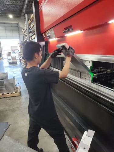 Operator aligning sheet metal on the press brake with back gauge support.