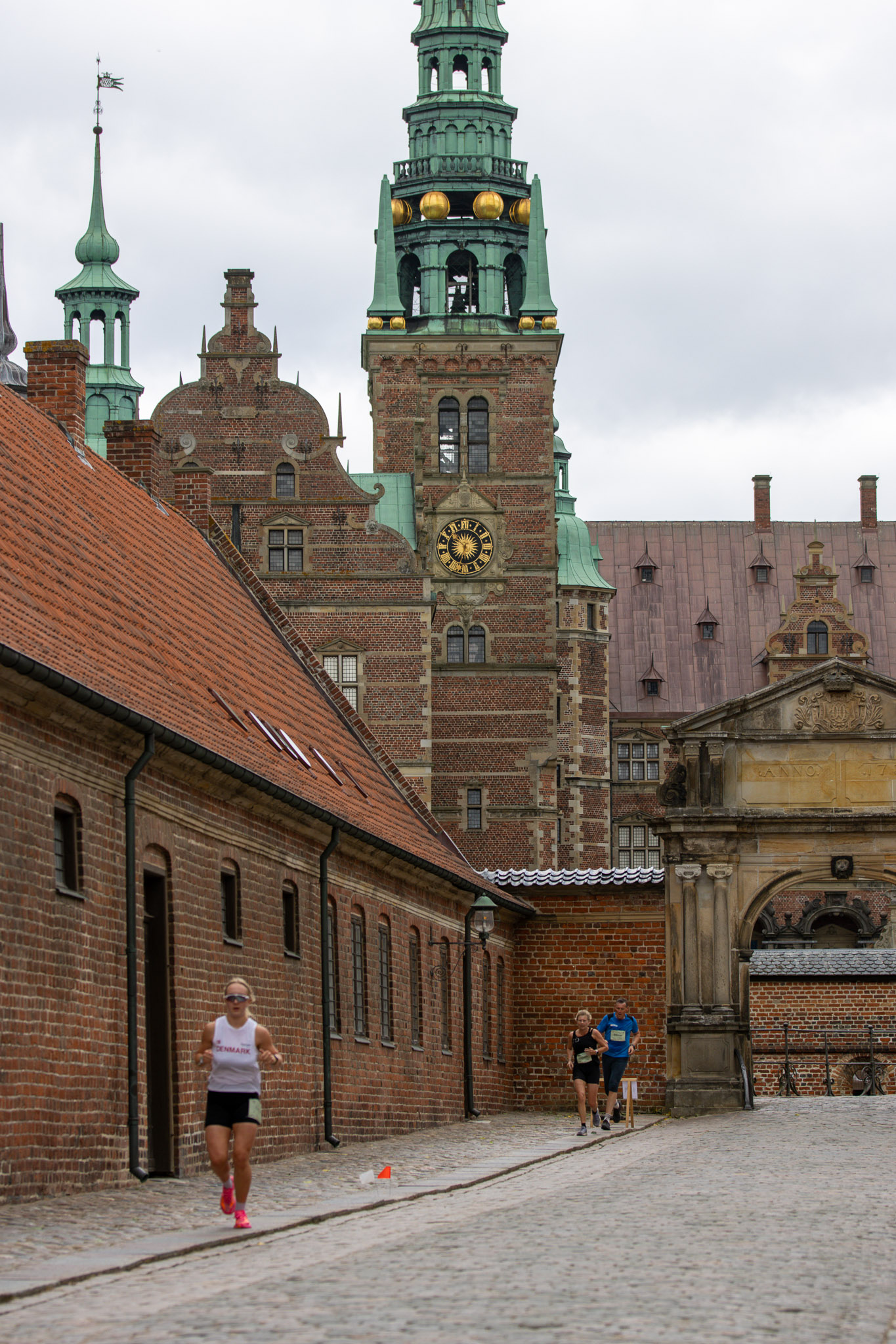 Tre løbere på brosten med Frederiksborg Slot i baggrunden.