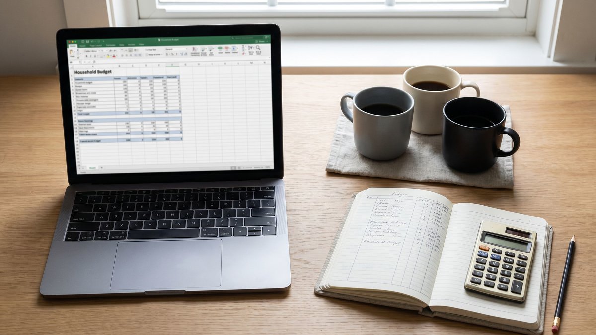 A laptop, notebook and three coffee cups on a roommate household budgeting desk