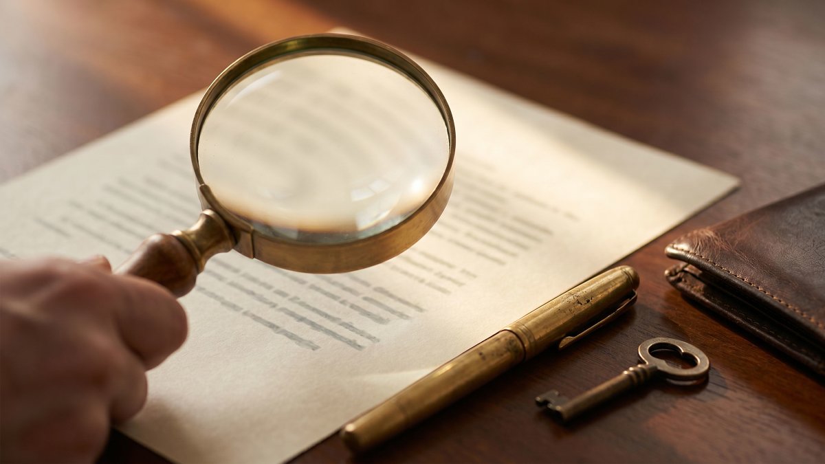Loupe en gros plan sur un contrat d'assurance, stylo doré et clé en bronze sur surface de bois ciré