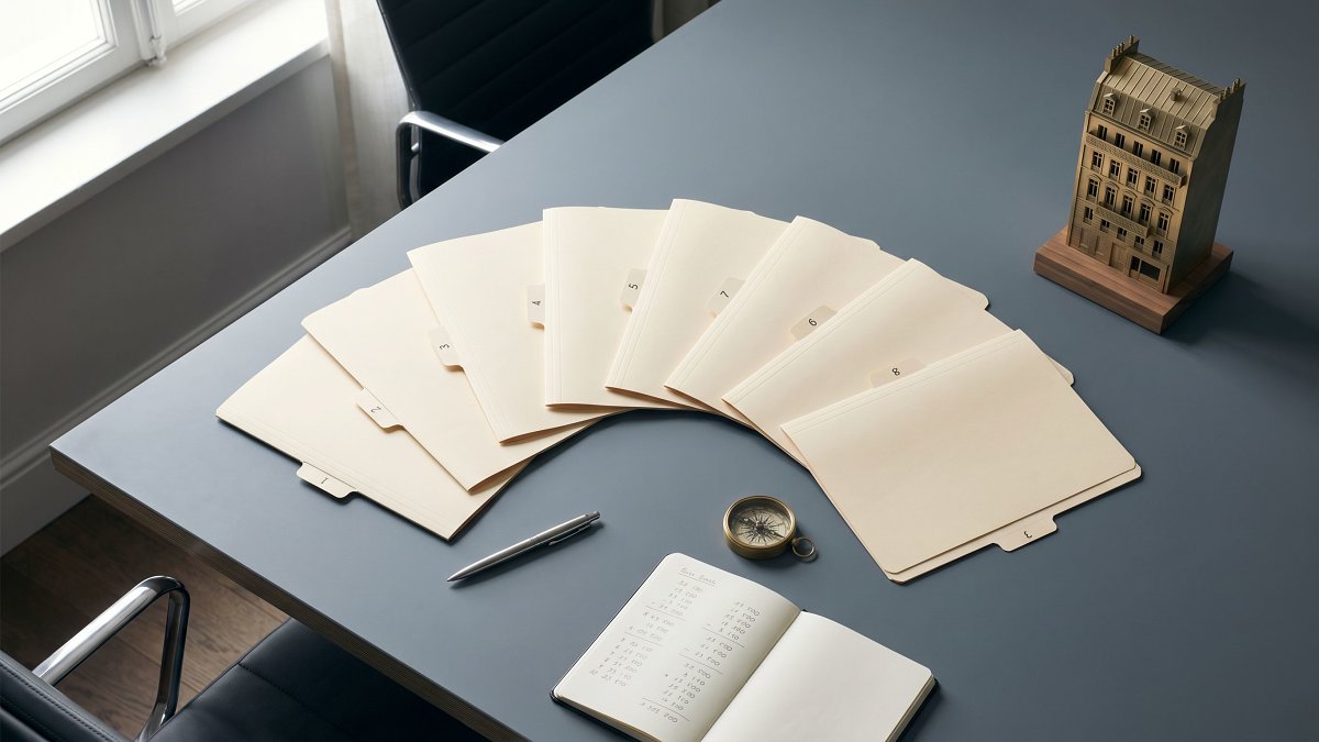 Huit dossiers de stratégie patrimoniale disposés en éventail sur une table grise avec compas et carnet