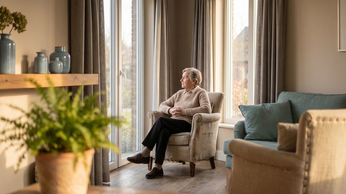 Personne assise dans un fauteuil près d'une fenêtre lumineuse, ambiance de recueillement et de pause