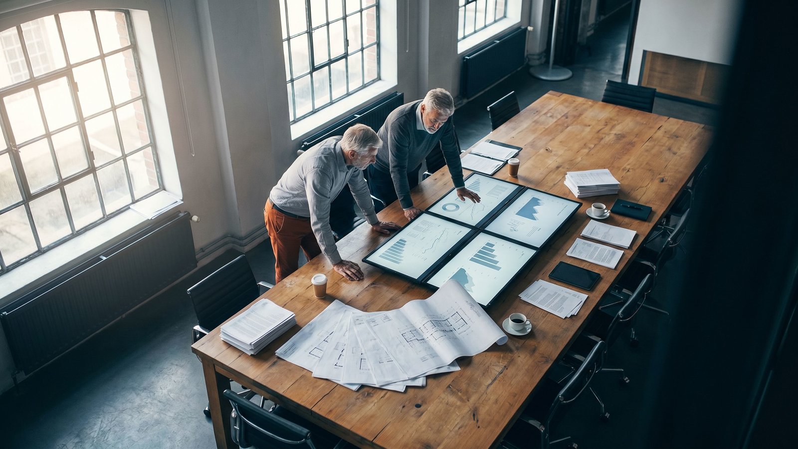 Two venture studio operators reviewing portfolio dashboards across an oak conference table in a studio operating room