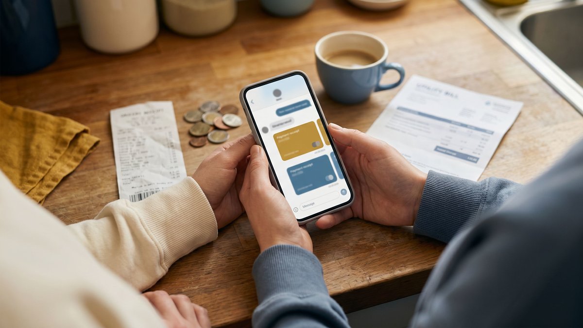 Four friends laughing around a kitchen table with a phone showing a shared expense ledger