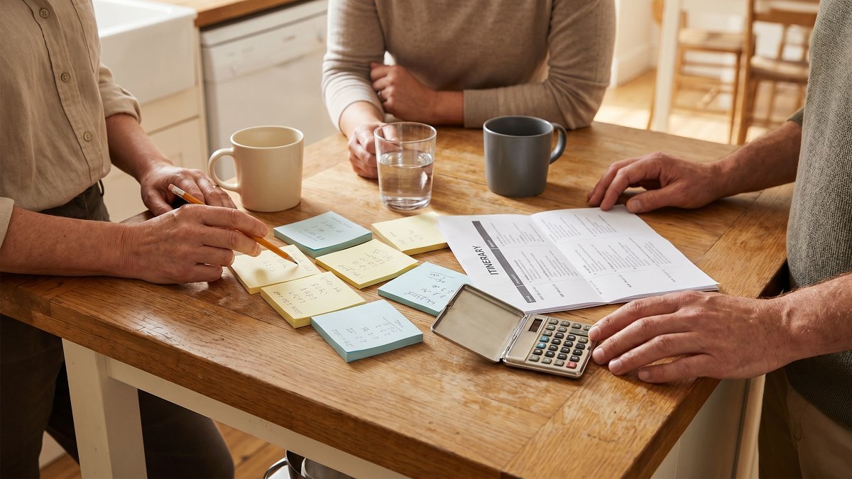 Friends sitting around a kitchen island writing expenses on sticky notes before a group trip