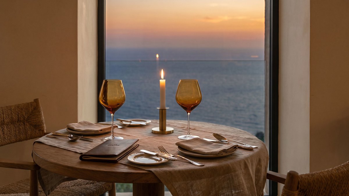 Linen-set table beside floor-to-ceiling Mediterranean window inside a kosher fine-dining room at sunset