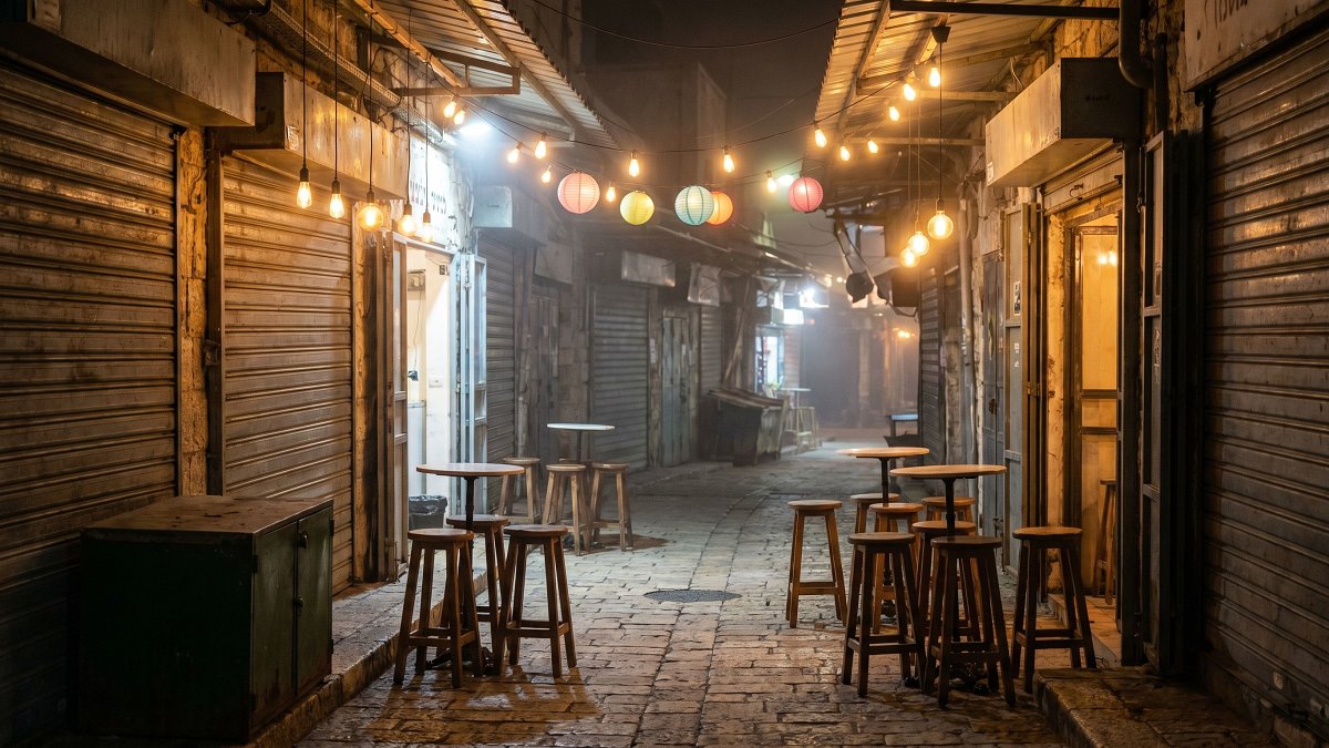 Machane Yehuda market lanes in Jerusalem at night with warm string lights and bar tables