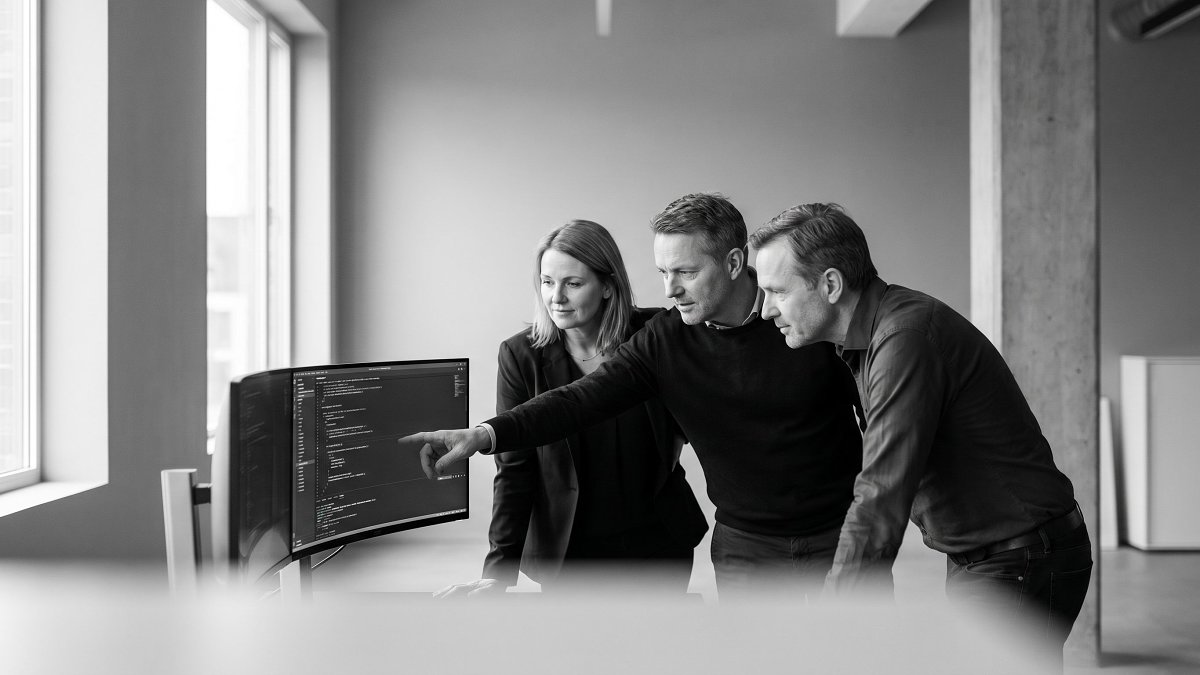 A small senior engineering team reviewing code together on one monitor, showing short communication lines