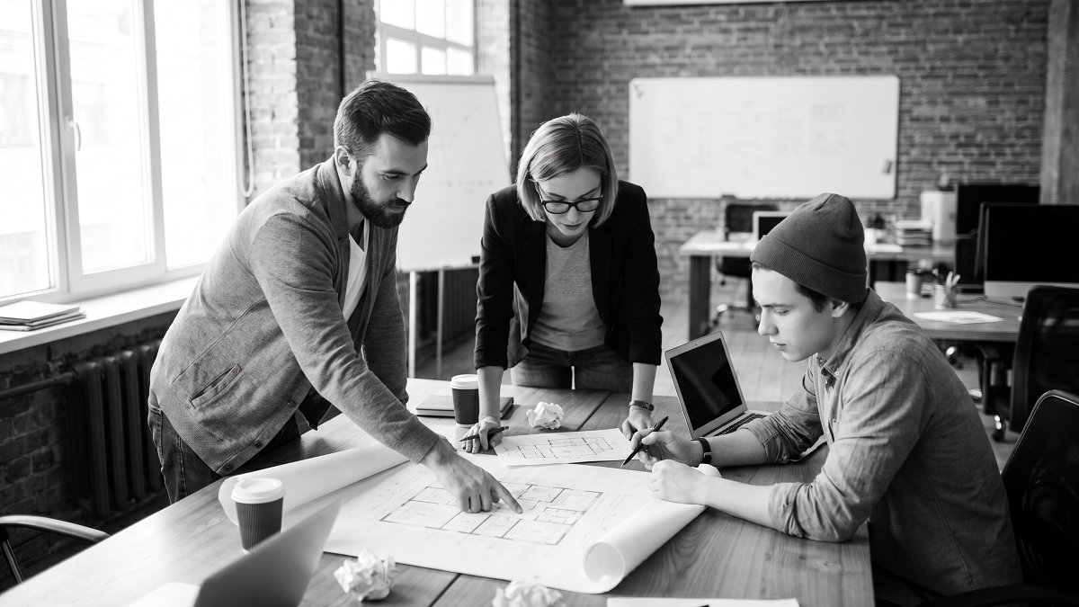 Founders and an engineer reviewing a printed build plan and architecture sketch