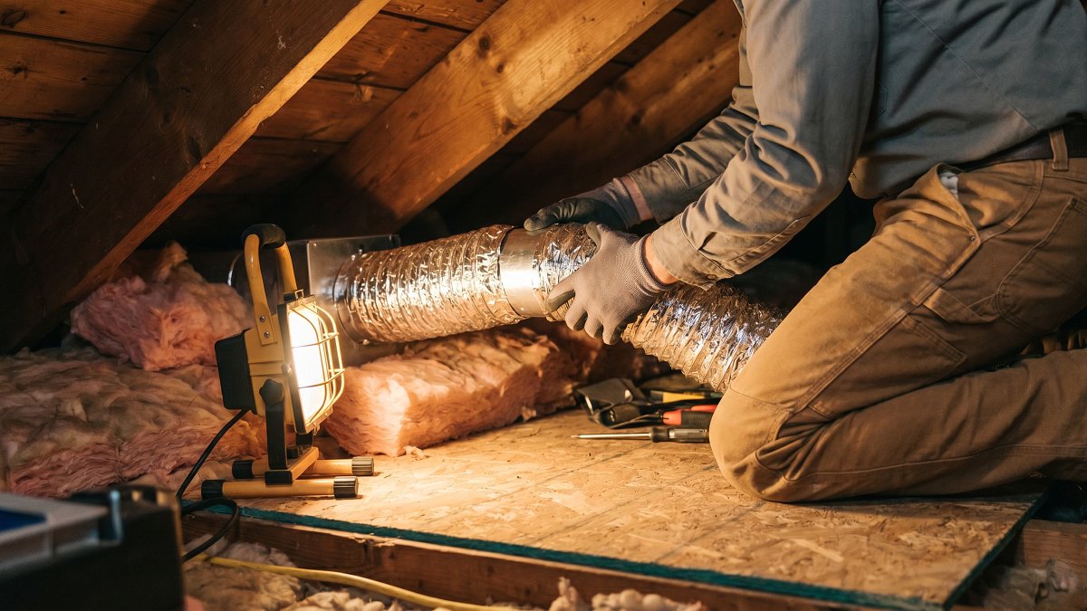 Artisan posant des gaines de ventilation dans des combles isolés