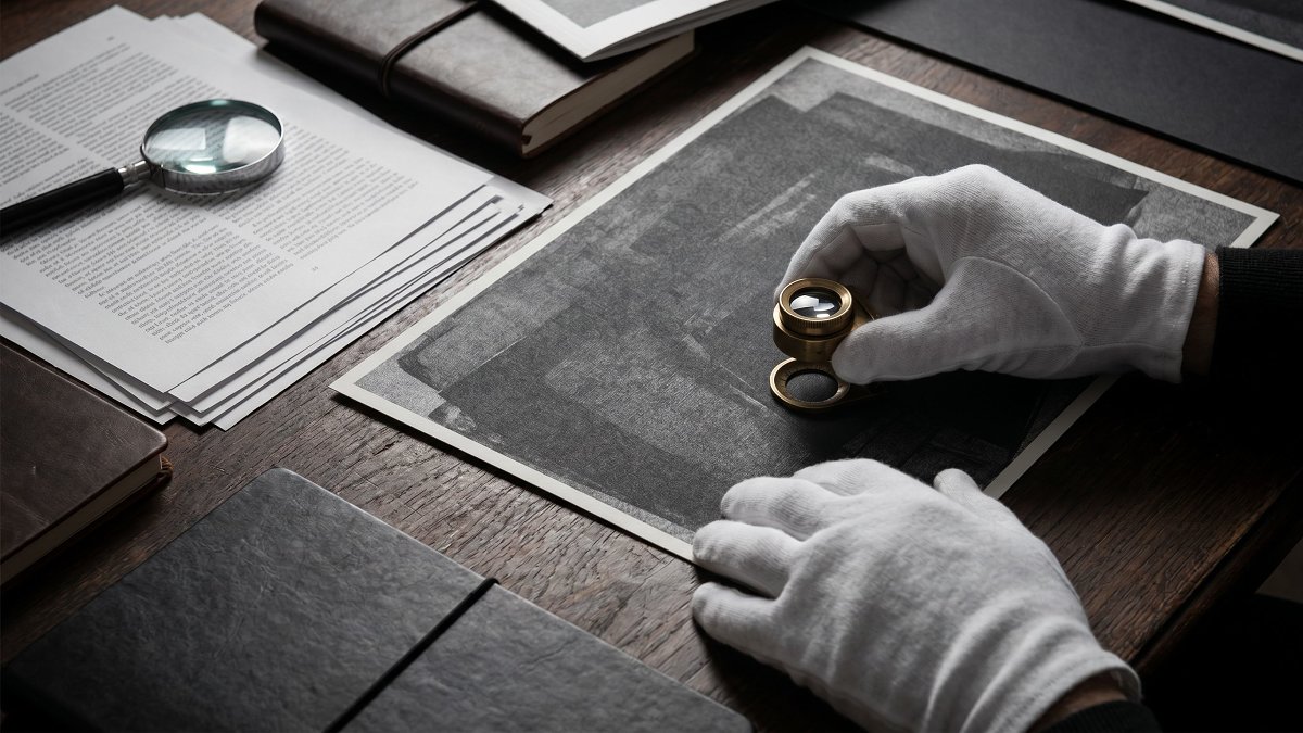 Gloved hands examining an artwork beside condition reports and provenance documents