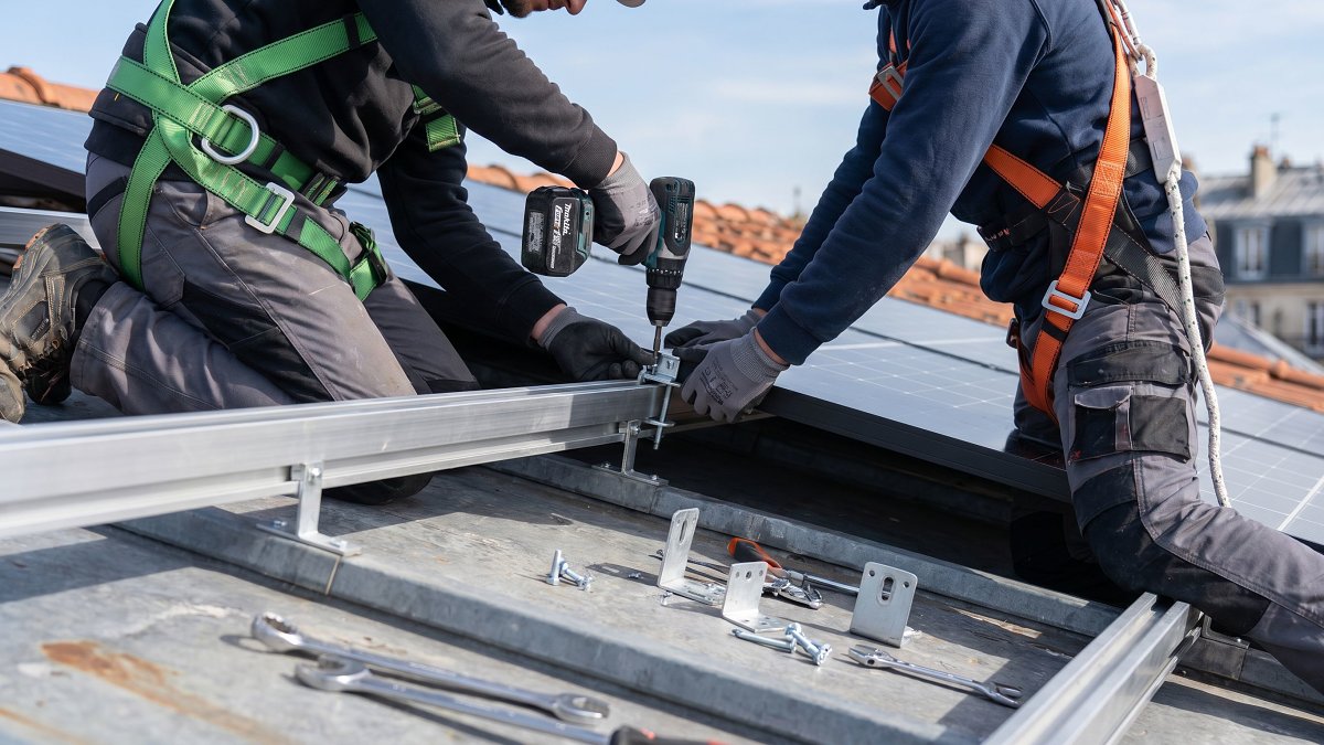 Installateurs fixant des modules photovoltaïques sur les rails d'une toiture tertiaire
