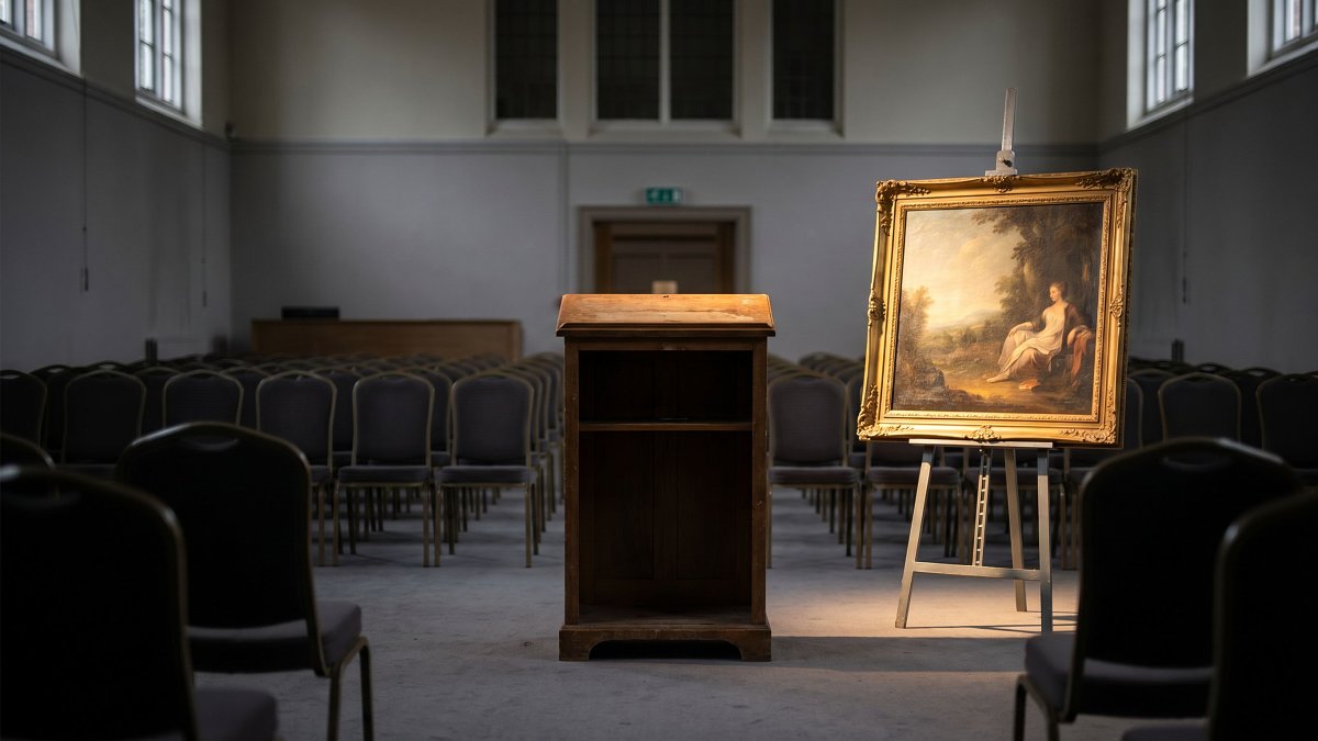 Salle des ventes aux enchères avec un tableau présenté sur un chevalet sous un projecteur