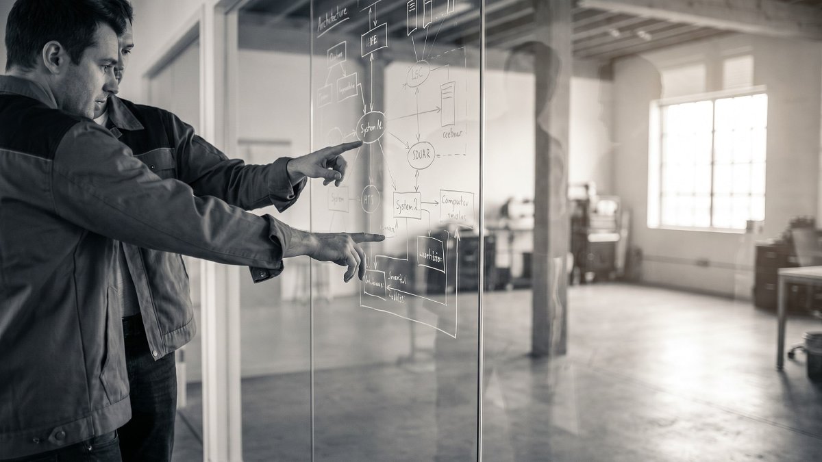 Two engineers reviewing a system architecture diagram on a glass wall during a rebuild