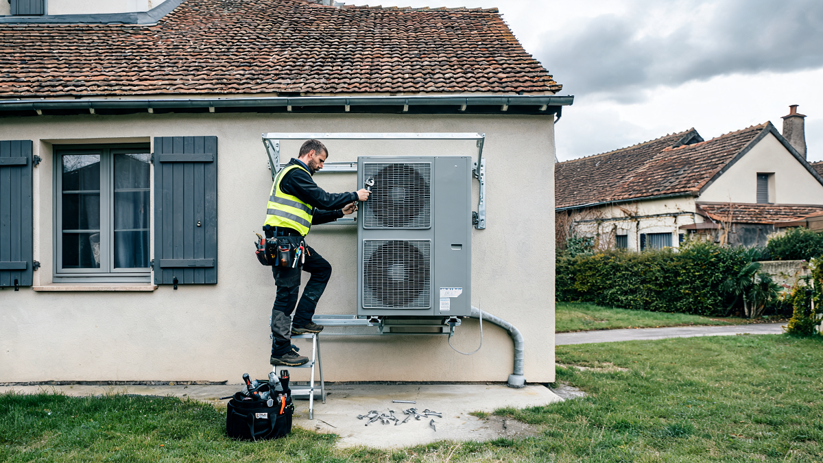 Technicien installant une pompe à chaleur air-eau sur la façade d'une maison en rénovation énergétique