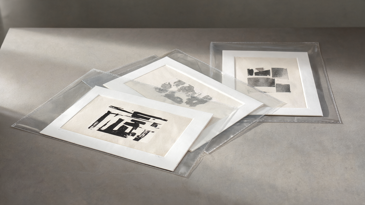 Unframed contemporary prints resting in protective sleeves on a conservator's table