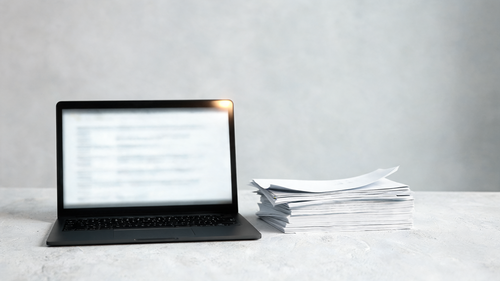 A laptop showing a plain Markdown file beside printed pages on a concrete desk