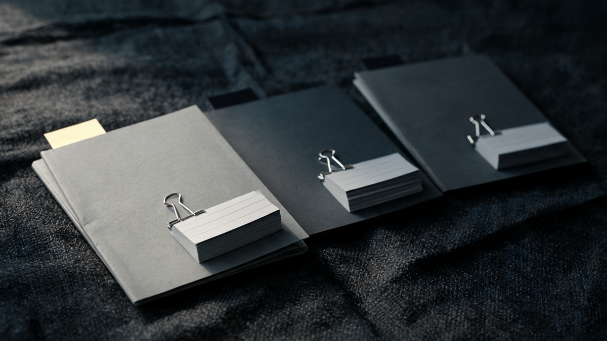 Three project dossiers fanned across a dark linen surface, one per studio engagement