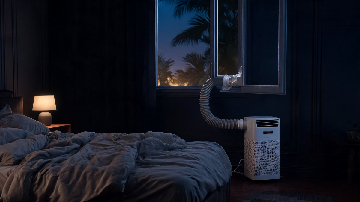 Climatiseur mobile monobloc en fonctionnement dans une chambre pendant une nuit de canicule, gaine passée par la fenêtre entrebâillée