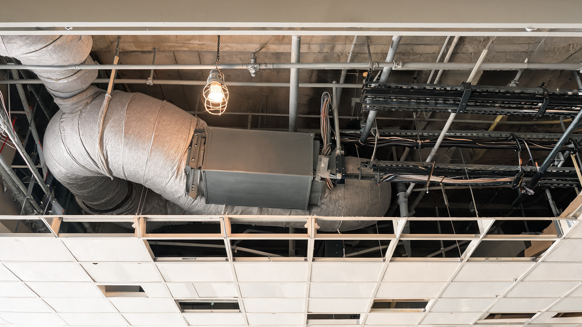 Plenum de faux plafond ouvert avec conduits d'air isolés, chemins de câbles et volet de désenfumage