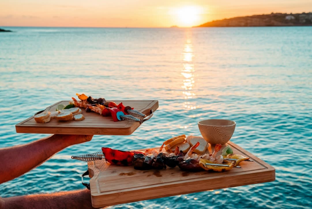 Two plates of food held over the water at sunset in Curaçao