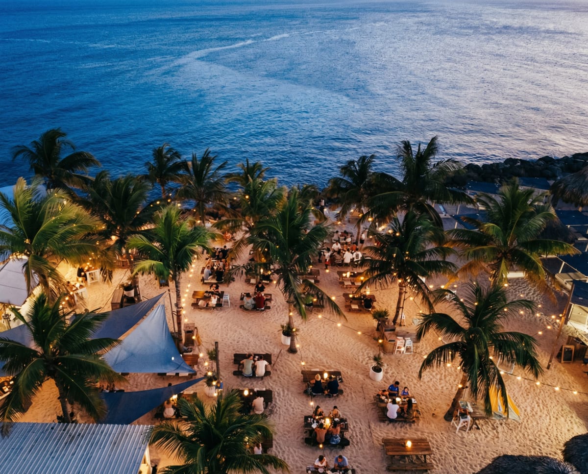Beachfront tables beneath palm trees at dusk in Curaçao