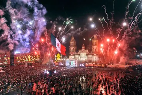 Zócalo lleno con fuegos artificiales y banderas.