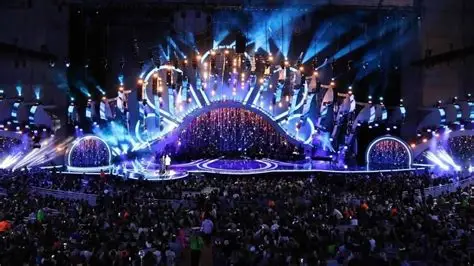 Escenario iluminado con miles de personas.