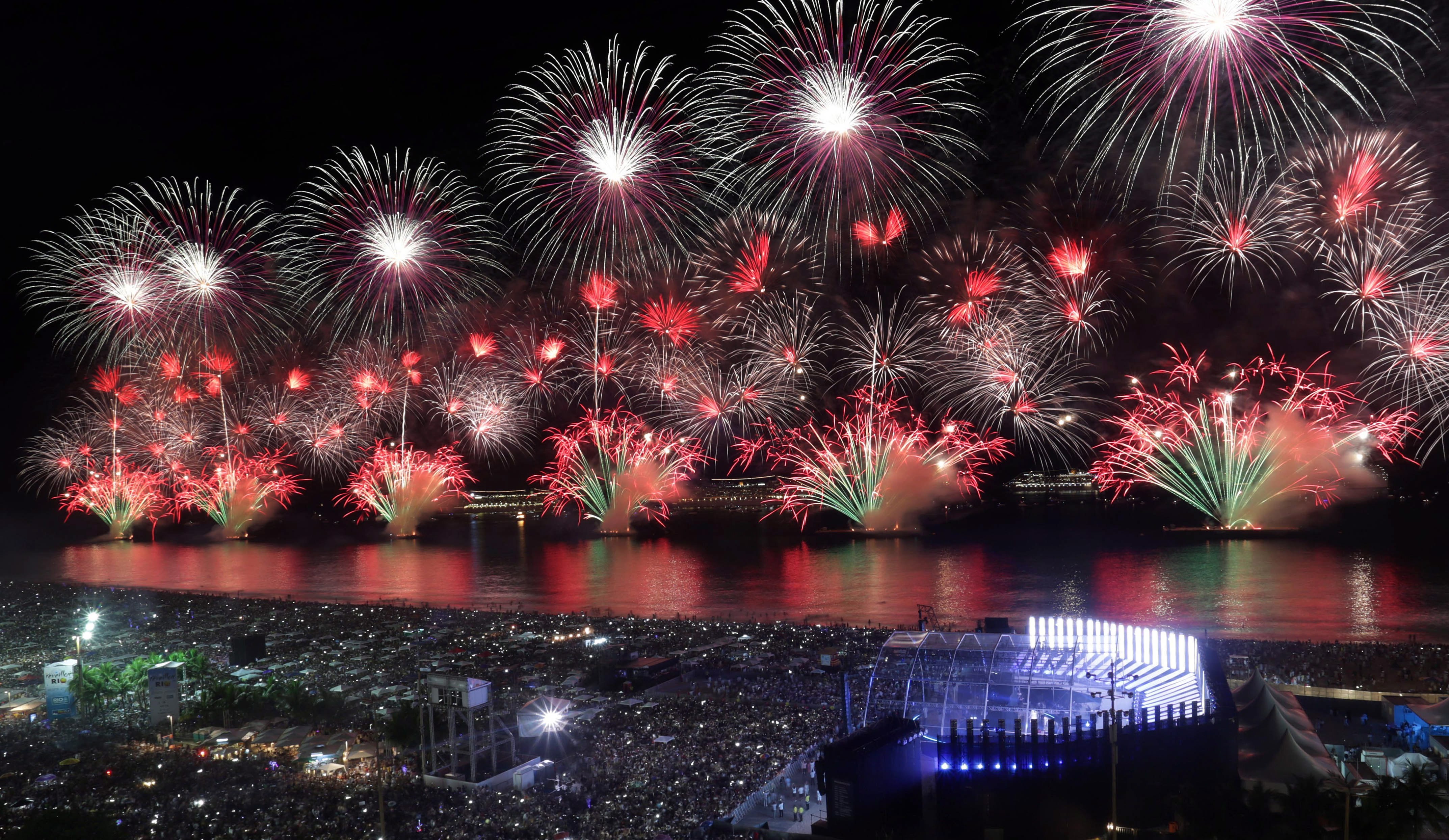 Fuegos artificiales sobre el mar y multitud en blanco.