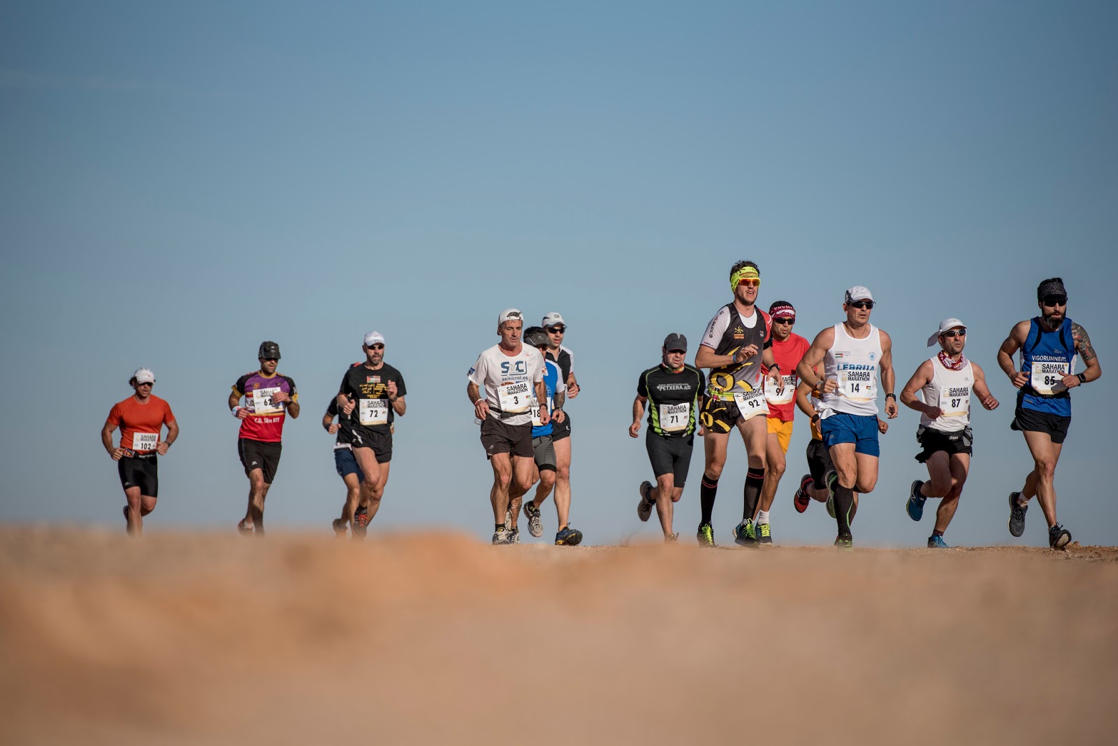 Corredores cruzando el desierto cerca de una mezquita de piedra.