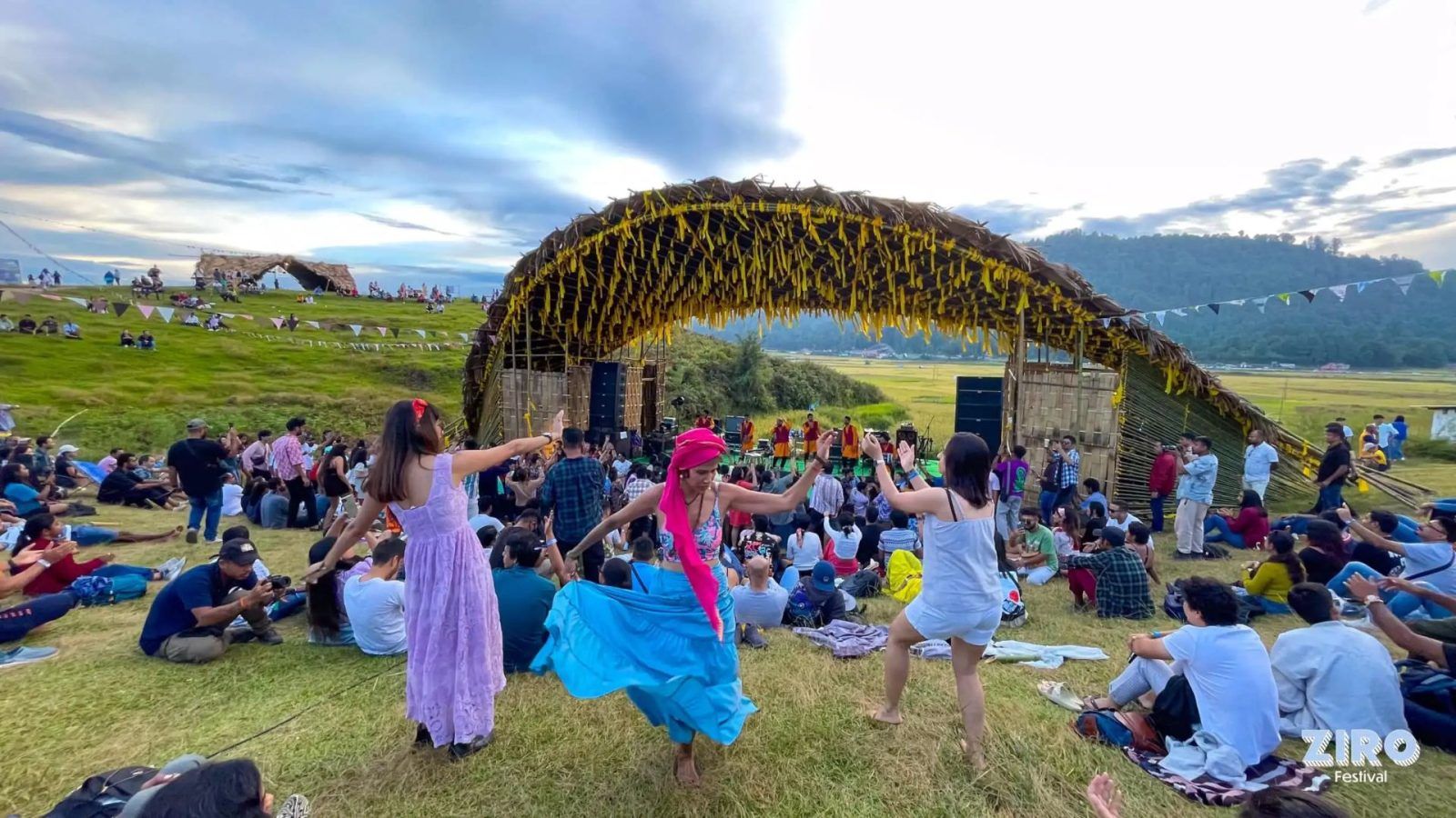 Gente acampando en un valle verde con música.