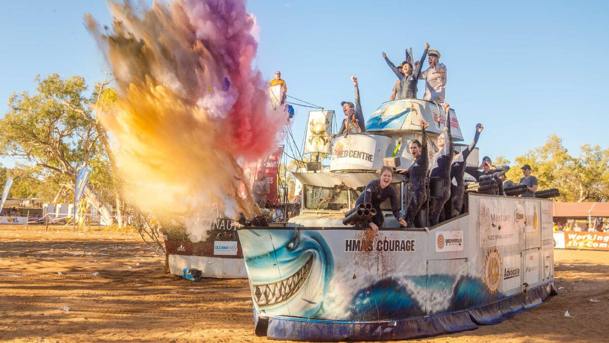 Gente corriendo con barcos de cartón por la arena.