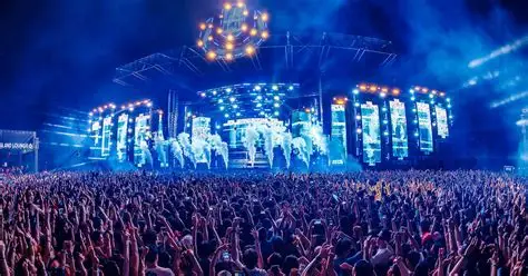 Escenario gigante con luces láser y público saltando.