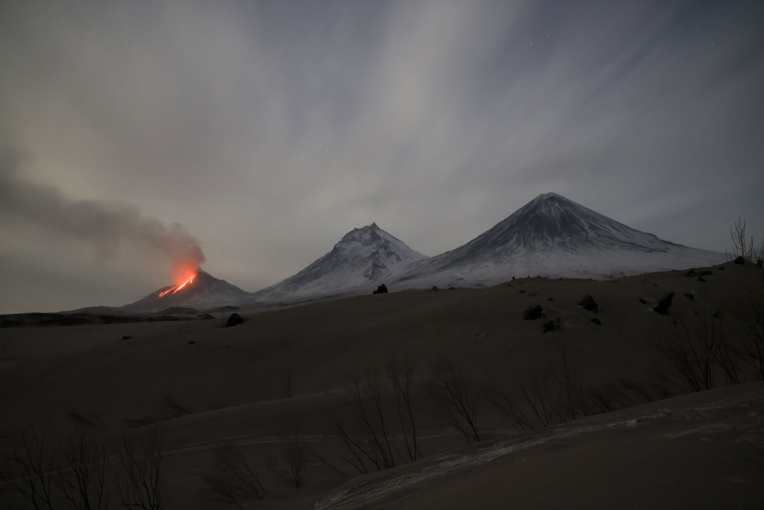 Volcán nevado con columna de humo bajo el sol.