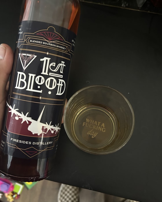 A hand holding a bottle of 1st Blood over a poured glass.