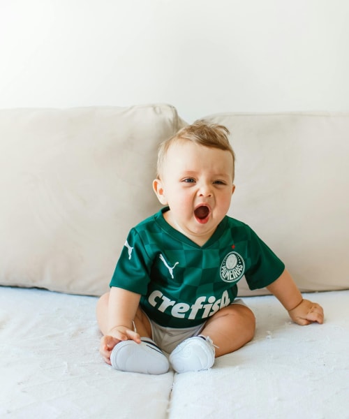 Cute baby wearing a green jersey yawning on a soft beige couch indoors
