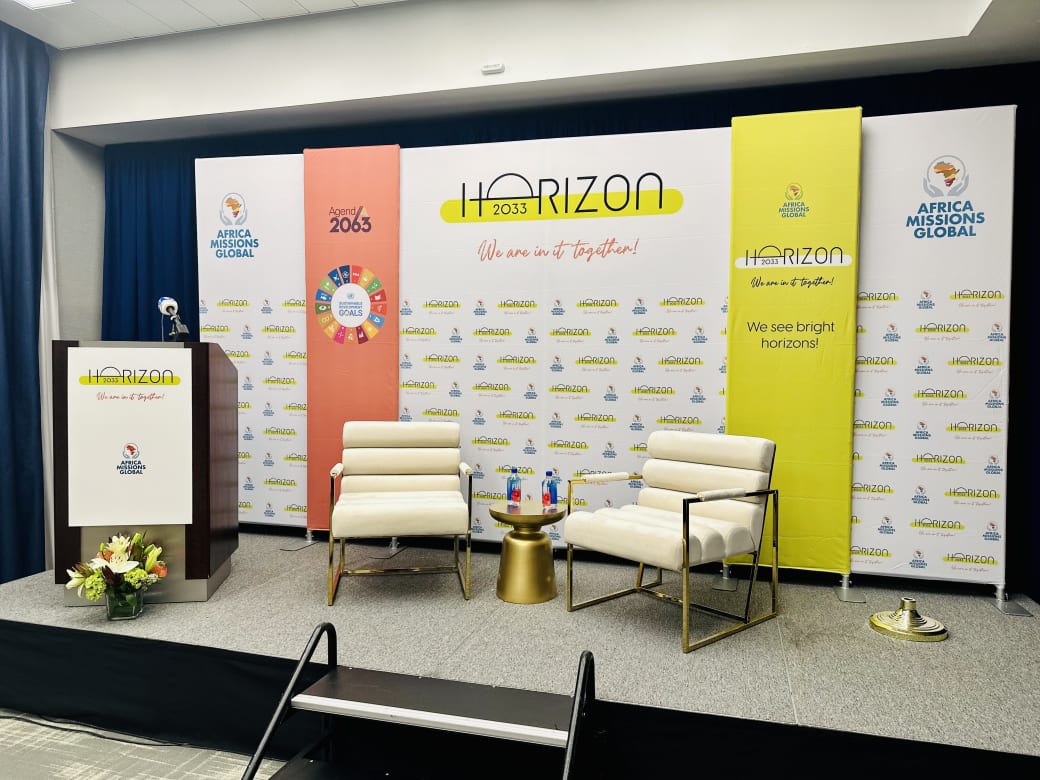 Horizon 2033 stage for Africa Missions Global with a step-and-repeat backdrop wall, orange and yellow fabric banners, and a branded podium sign